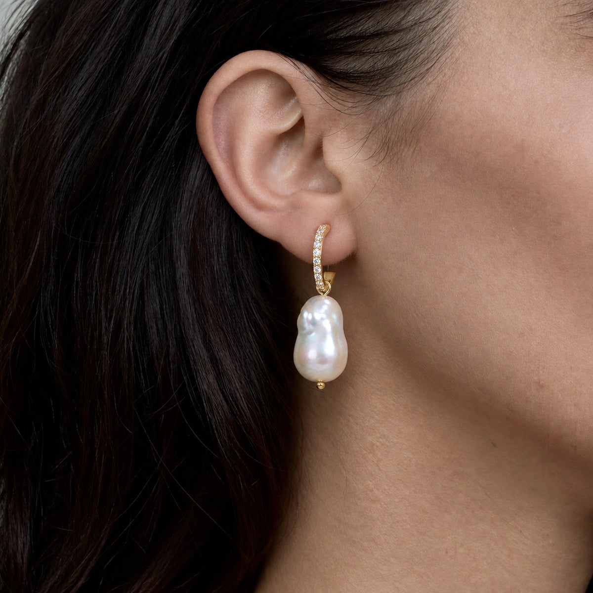 Close-up of a gold pave hoop earring with a white baroque pearl drop