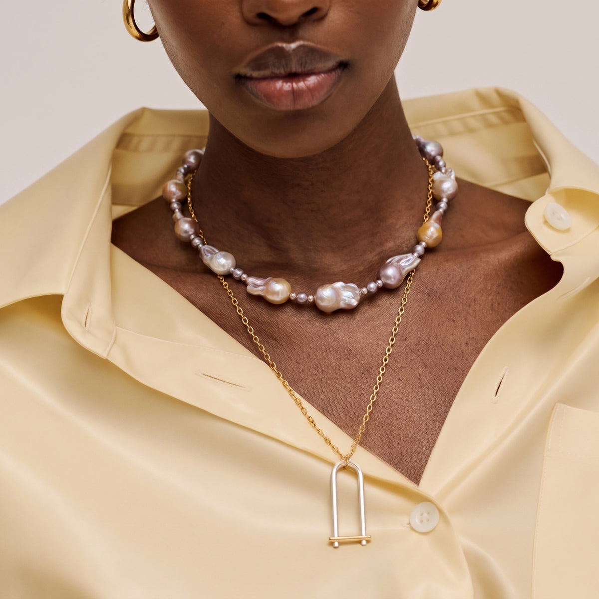 Woman wearing a multicolor baroque pearl necklace with a geometric silver pendant on a gold chain