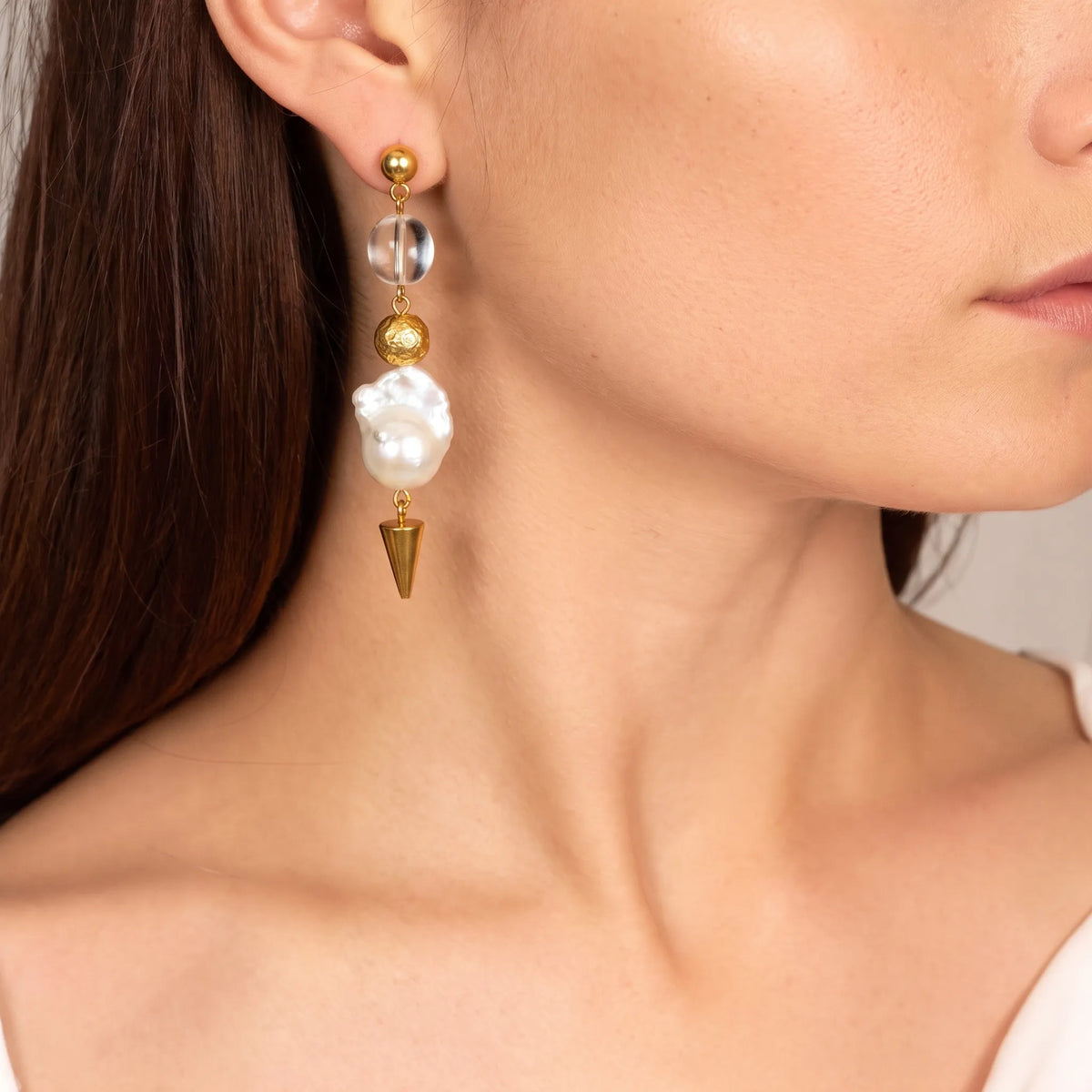 Close-up of a crystal and baroque pearl drop earring with gold ball stud and cone pendant