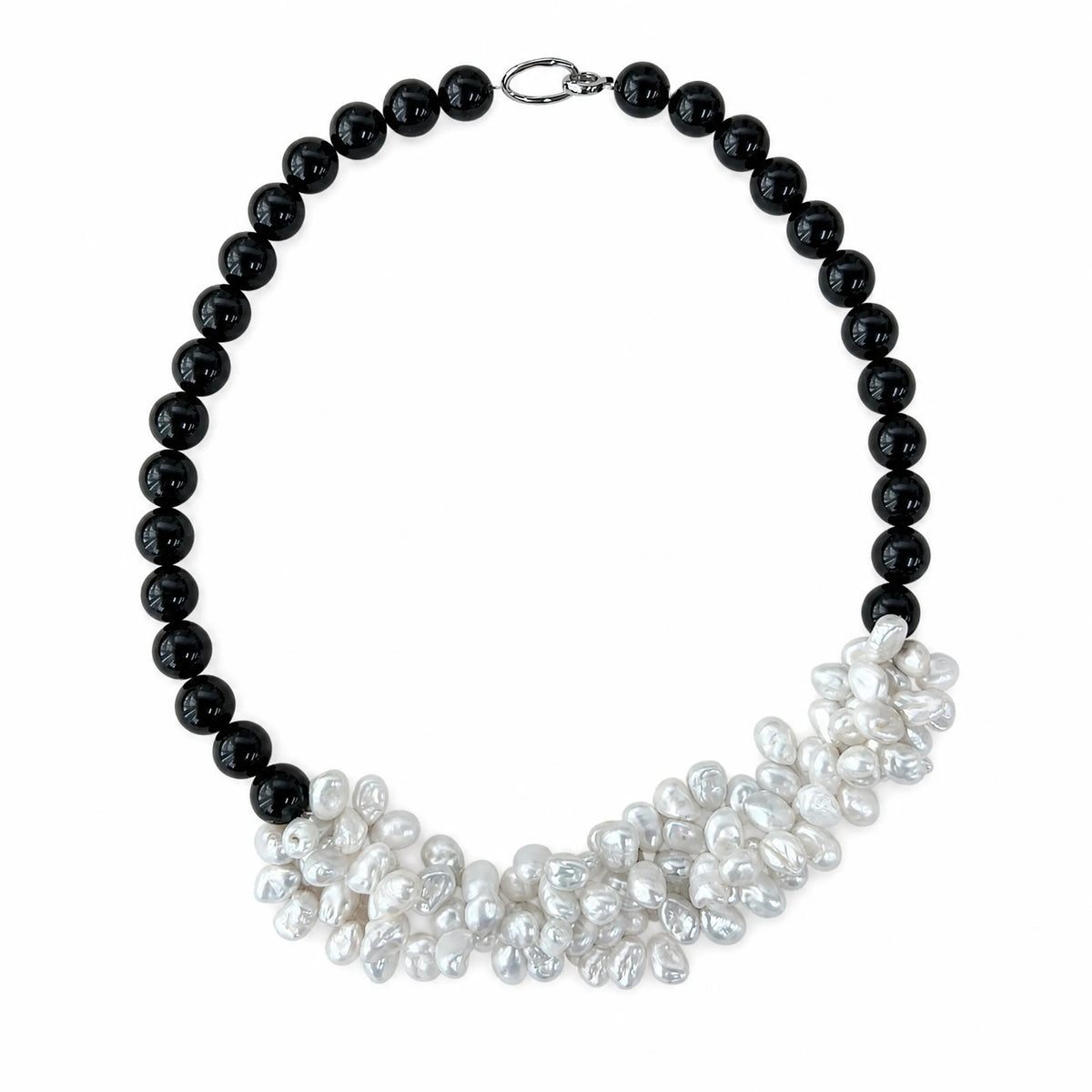 Black onyx beaded necklace with a cluster of white petal-shaped baroque pearls, flat lay on white background