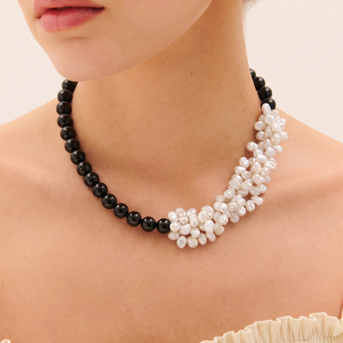 Woman wearing a black onyx and petal-shaped baroque pearl layered necklace