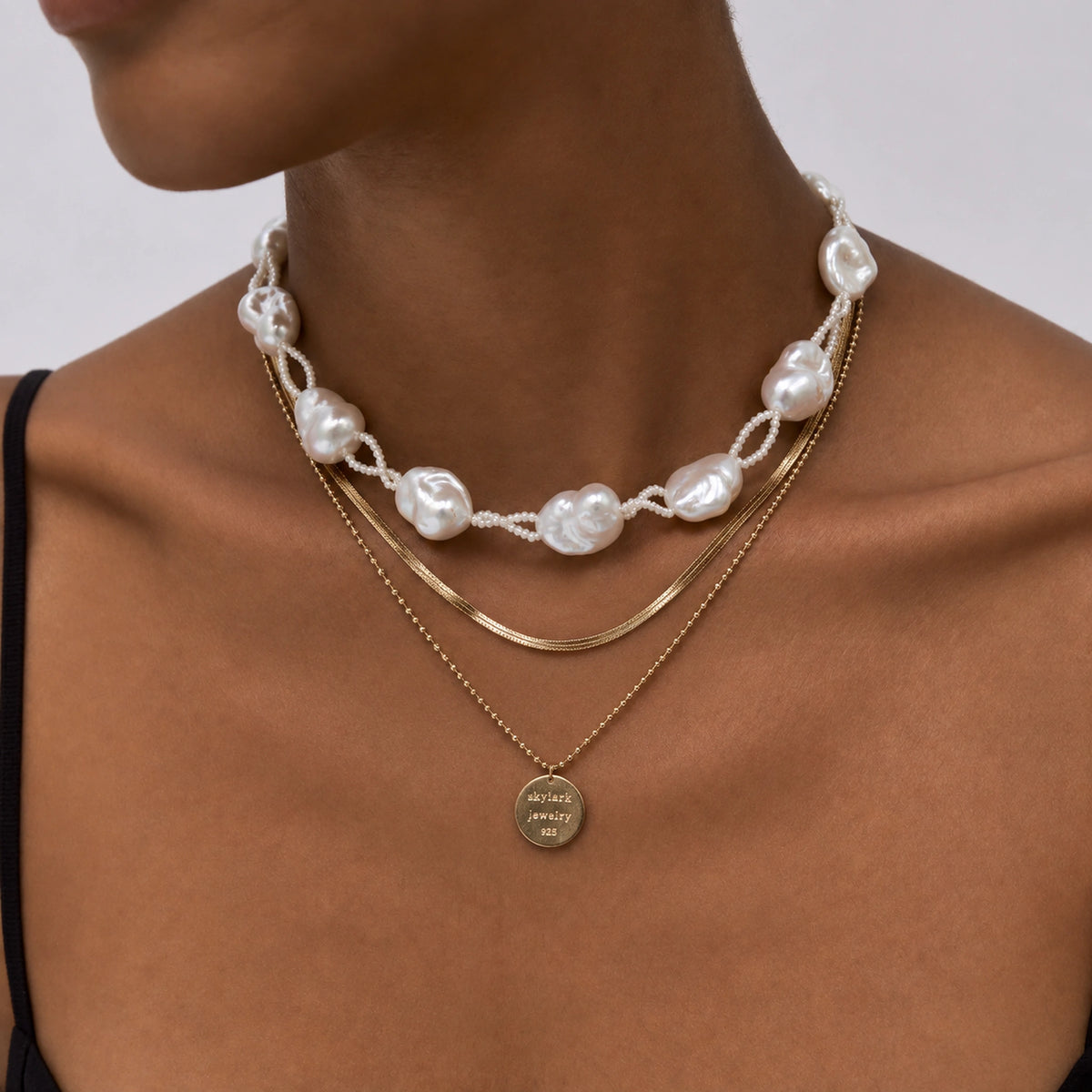 Woman wearing a layered necklace with baroque pearls, gold chains, and a round gold pendant tag