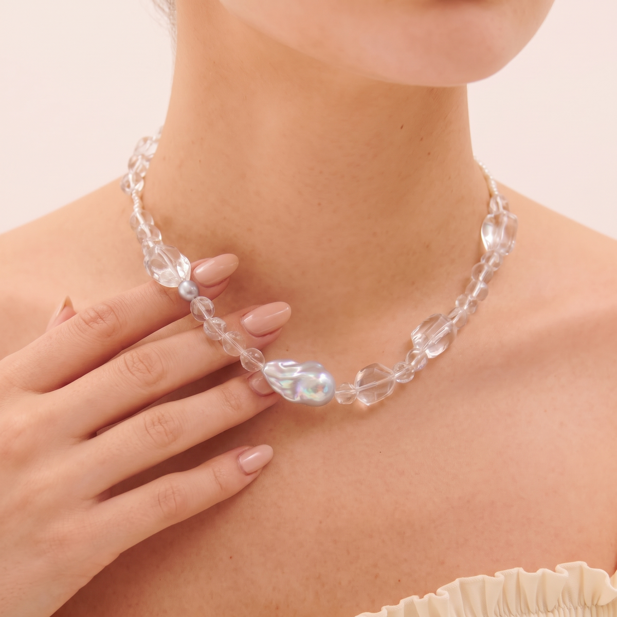 Close-up of fingers touching a grey baroque pearl and faceted beads on a necklace