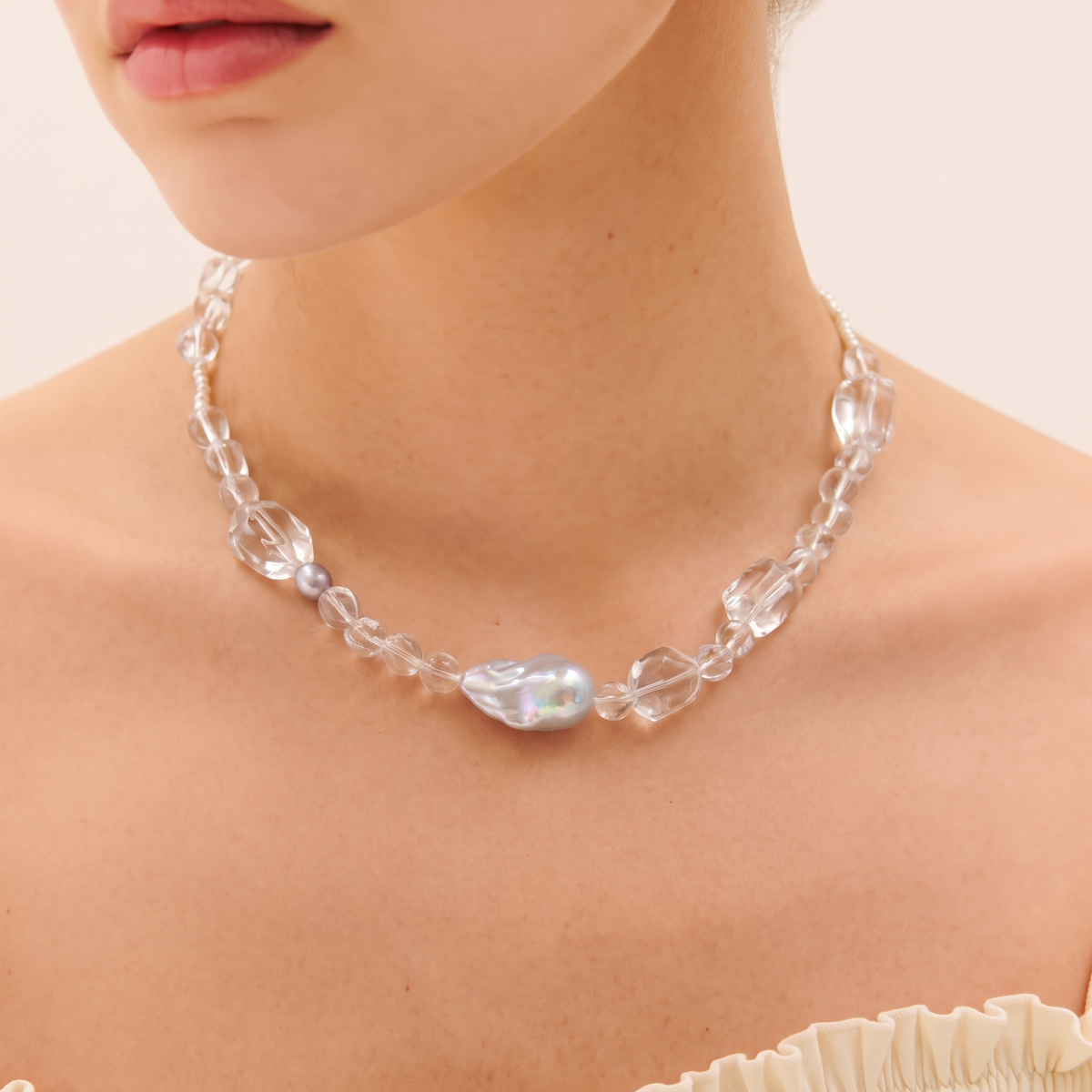 Woman wearing a necklace with faceted clear beads and a large grey baroque pearl