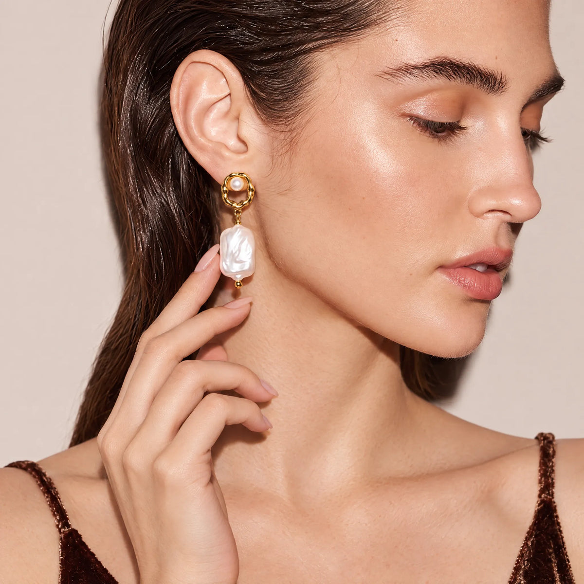 Close-up of fingers touching a scalloped gold frame earring with a baroque pearl drop