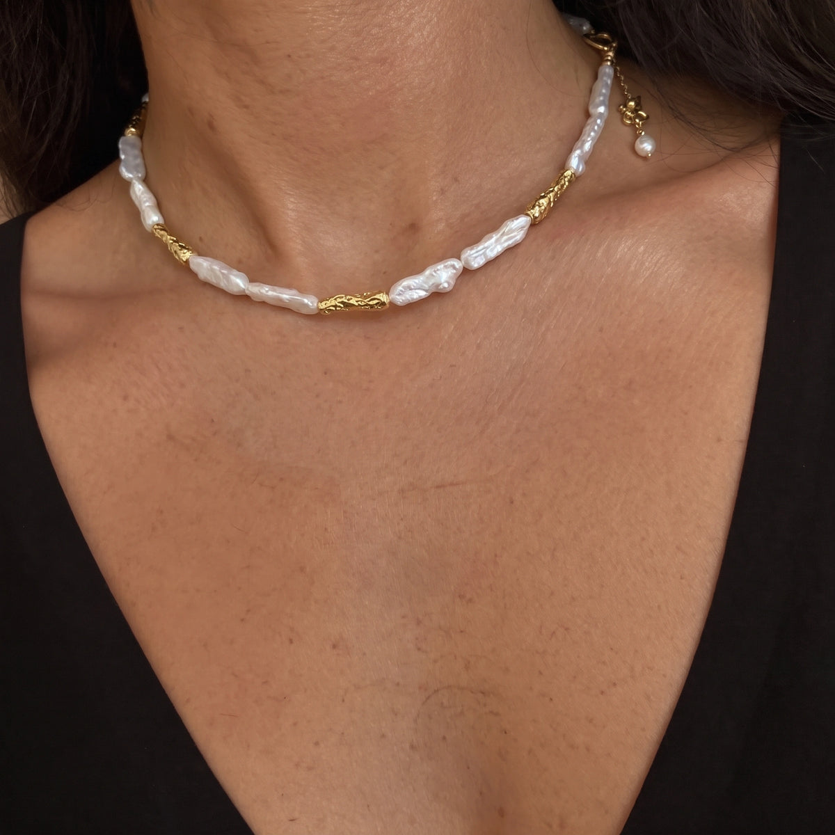 Woman wearing a necklace with elongated baroque pearls alternating with textured gold reed-shaped links