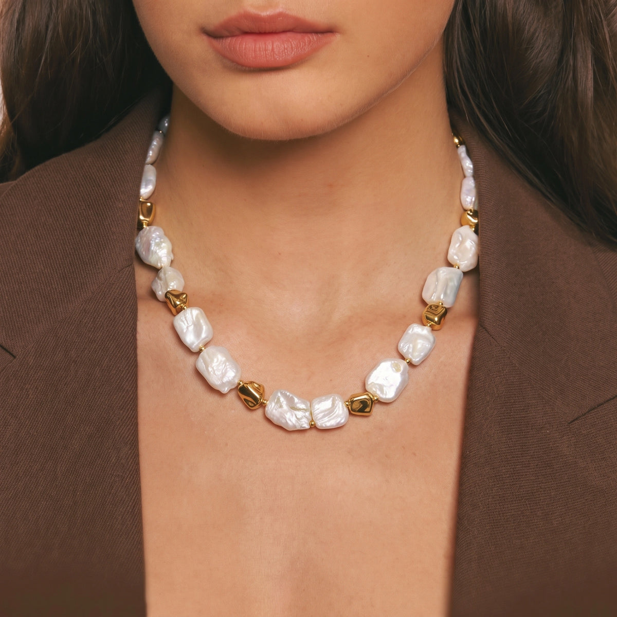 Close-up of a necklace with square baroque pearls and gold stone-shaped links, worn with a brown jacket