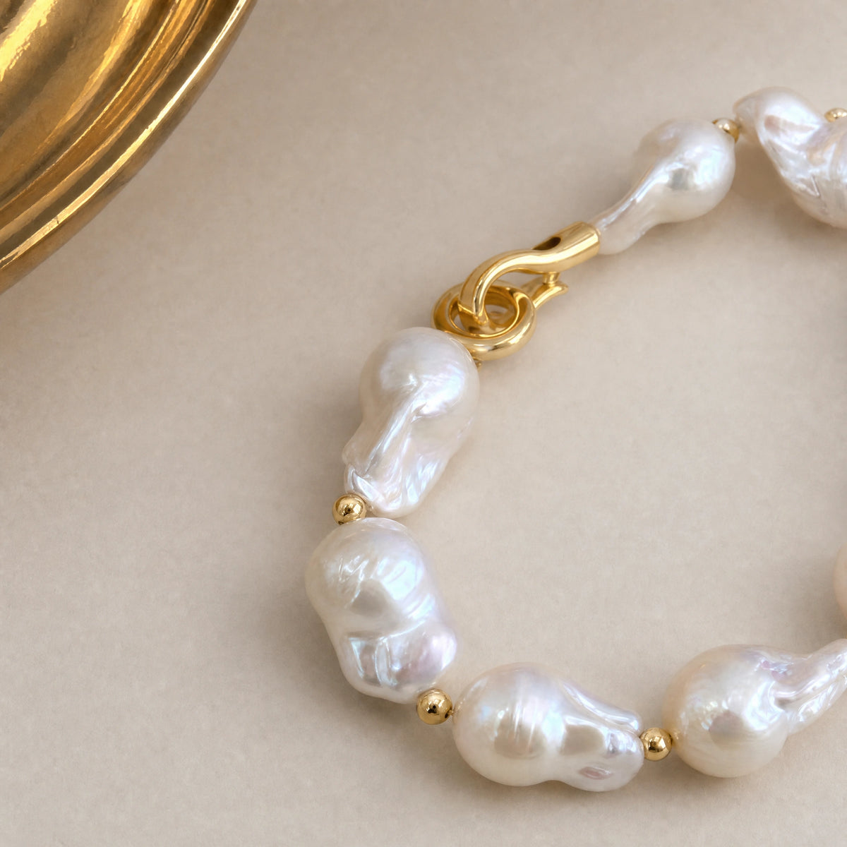 Close-up of a gold S-hook clasp on a baroque pearl bracelet with teardrop pearls
