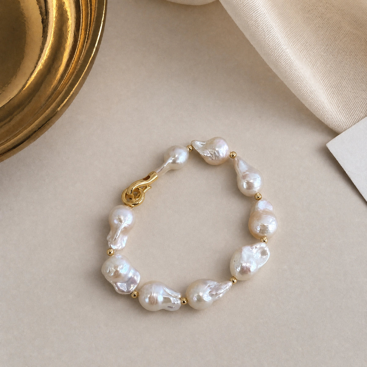 Golden Current baroque pearl bracelet laid flat in a circle, with teardrop pearls and a gold hook clasp