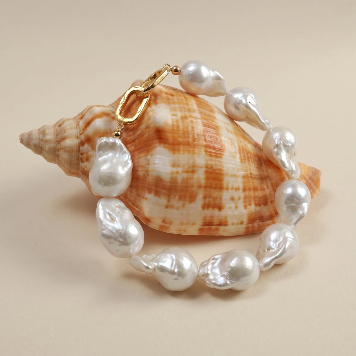 Large baroque pearl bracelet laid flat in a circle next to a striped seashell