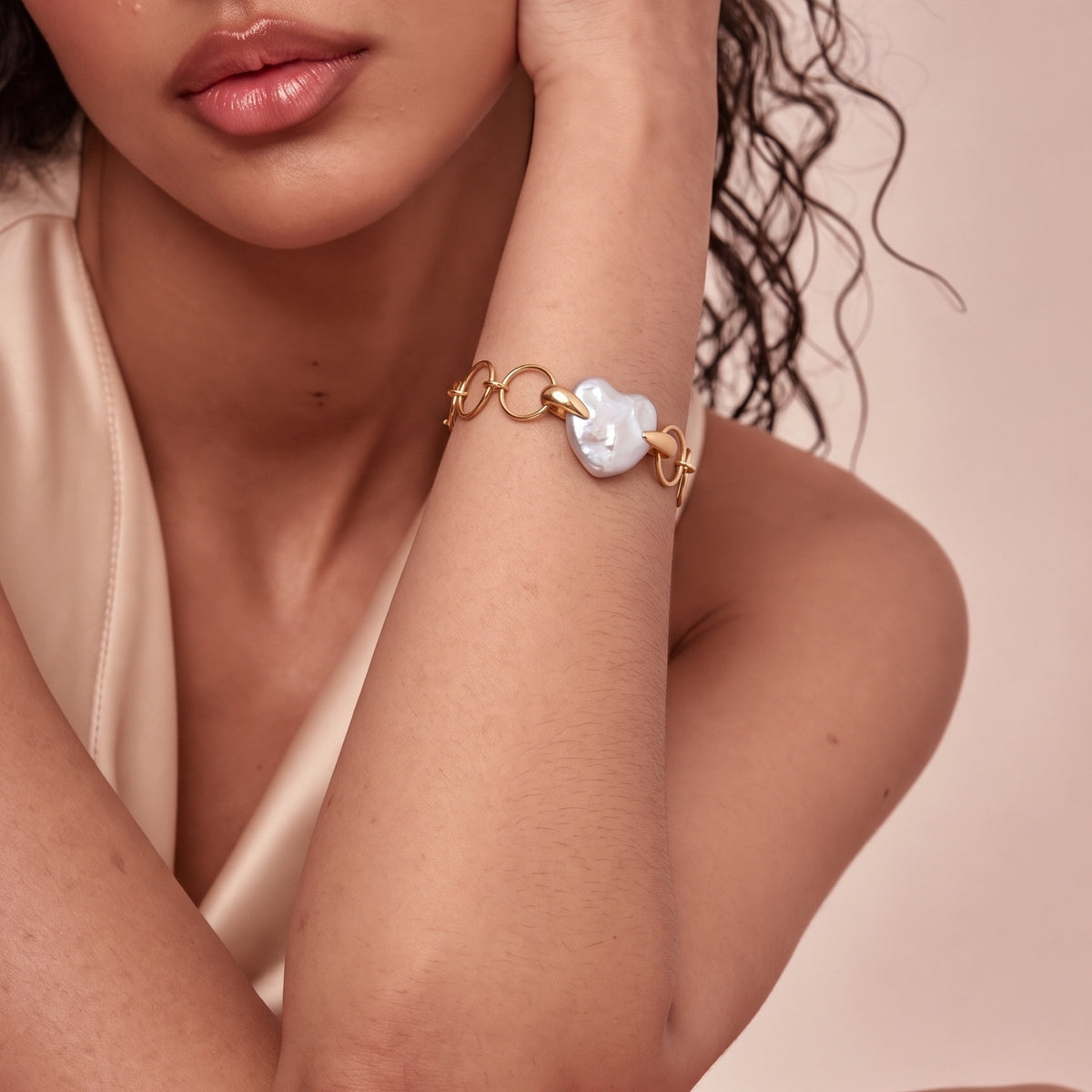 Woman wearing a gold chain bracelet with a heart-shaped pearl charm, arm raised