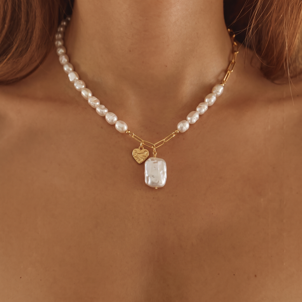 Close-up front view of a necklace with pearls, gold links, and a heart tag pendant