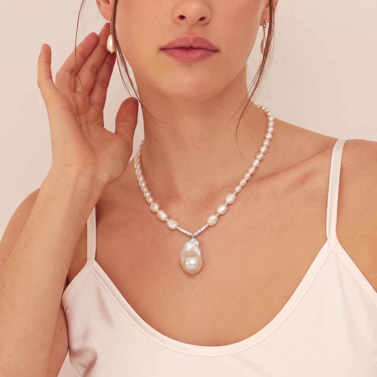 Woman wearing a necklace with irregular white baroque pearls and silver crystal links, with a large pearl pendant