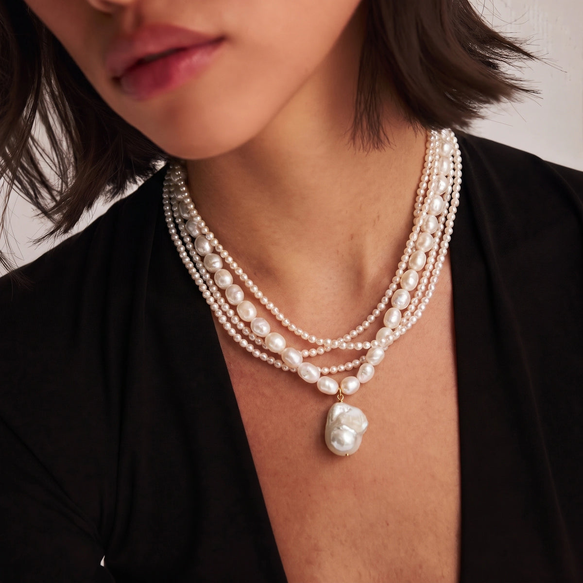 Close-up of a layered necklace with multiple pearl strand textures and a large baroque pearl pendant