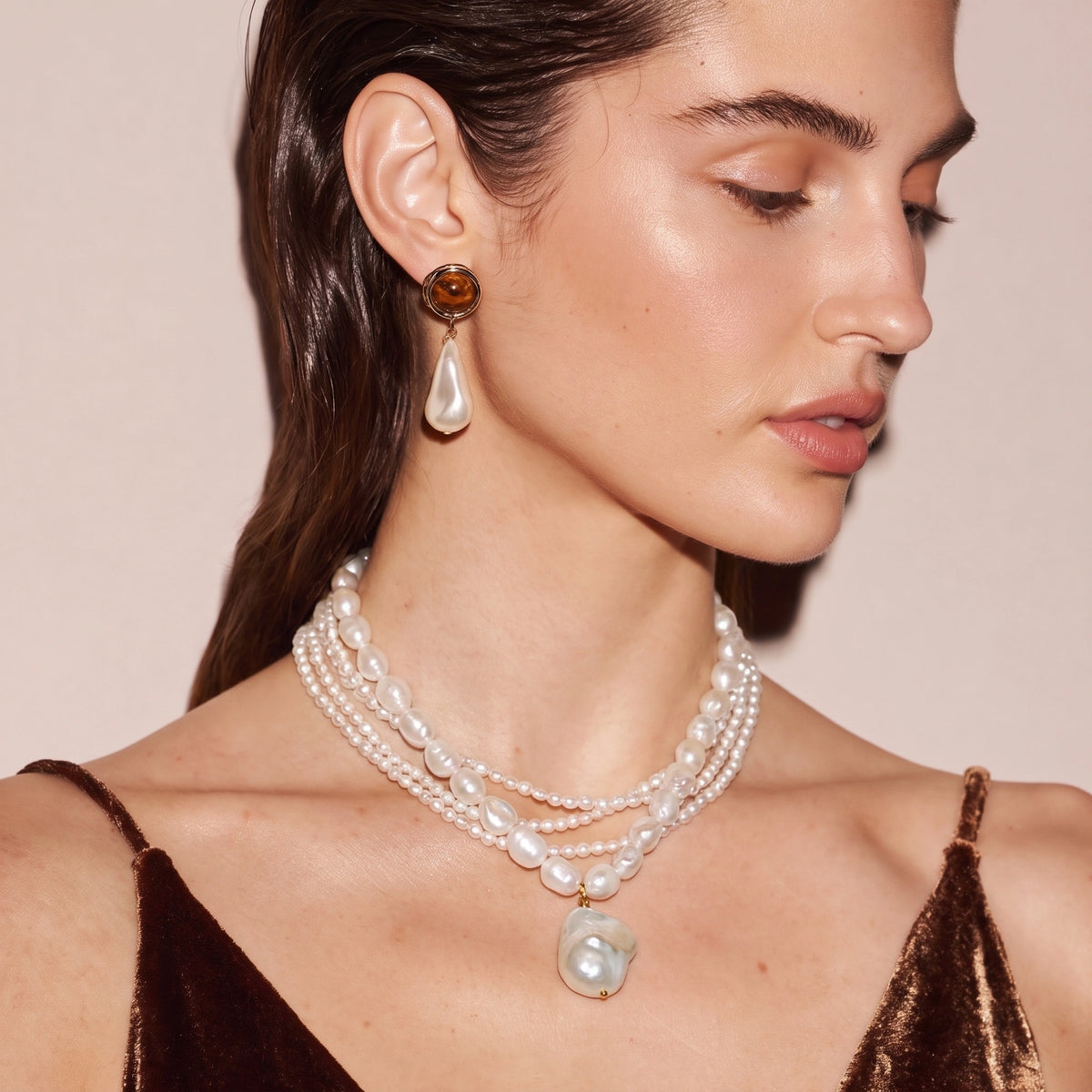 Woman wearing a layered baroque pearl necklace with enamel hoop earrings and a teardrop pearl earring