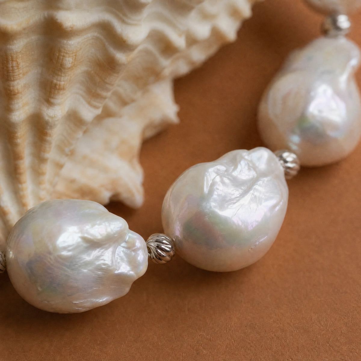 Close-up of baroque pearls and engraved silver spacer beads on a bracelet, with a seashell in the background