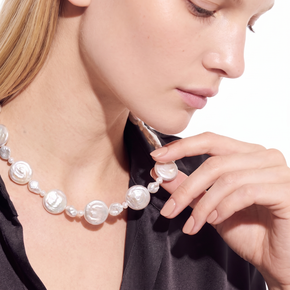 Woman wearing a graduated white pearl necklace, touching her neck, side angle