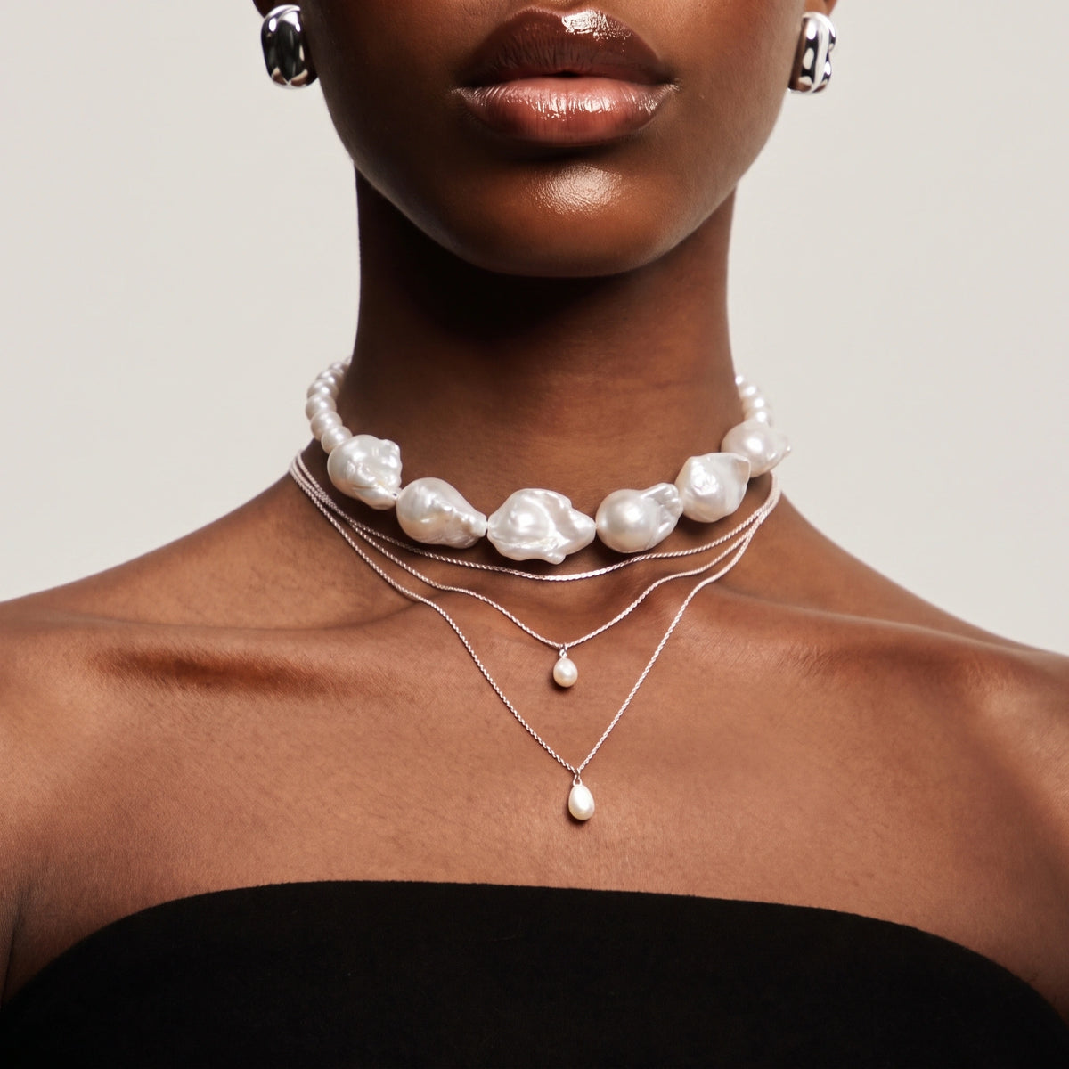 Woman wearing a large baroque pearl necklace layered with two thin chains and teardrop pearl charms