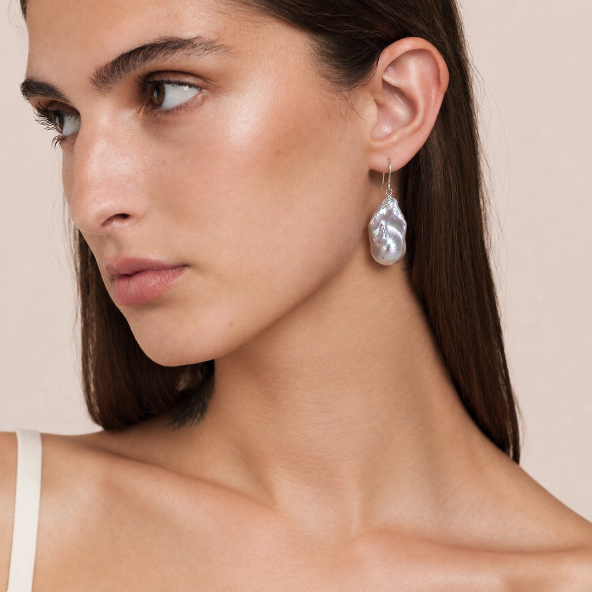 Close-up of a silver-white baroque pearl drop earring on a thin silver hook