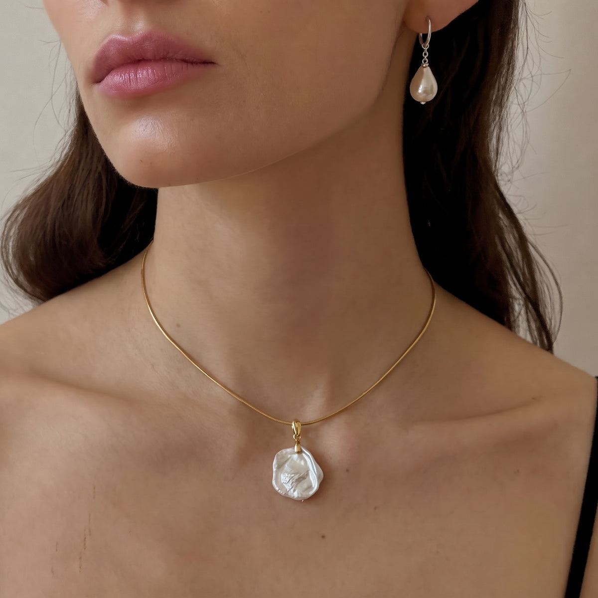 Close-up of a gold chain choker with a baroque pearl pendant, with matching teardrop pearl earring
