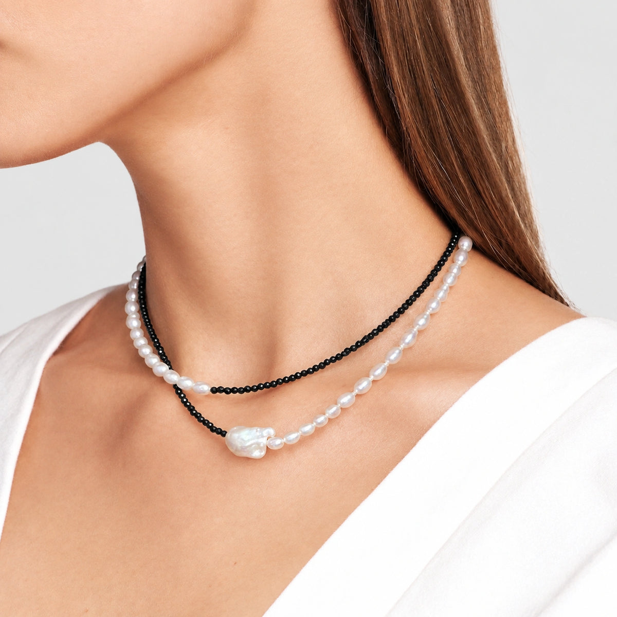 Woman wearing a double-layer necklace with black beads and white baroque pearls