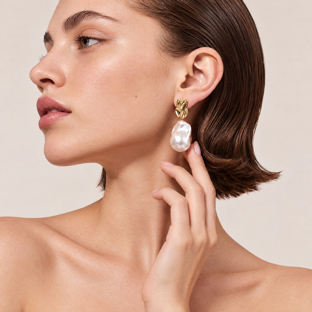 Close-up of a wavy gold sculptural earring with a large irregular baroque pearl drop