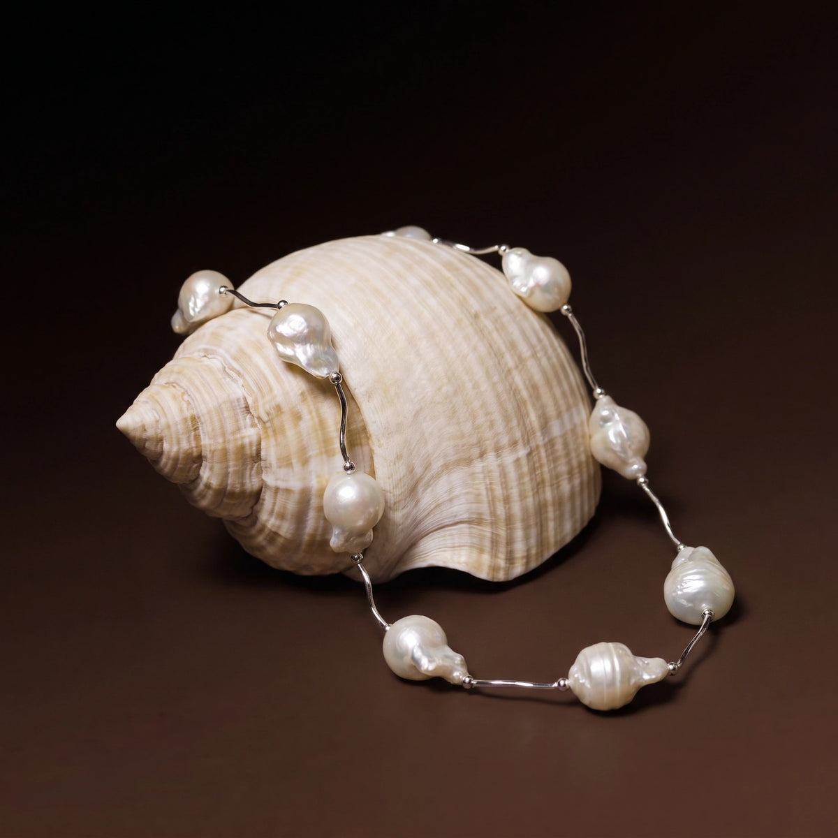 Silver tube link necklace with baroque pearls draped over a spiral seashell