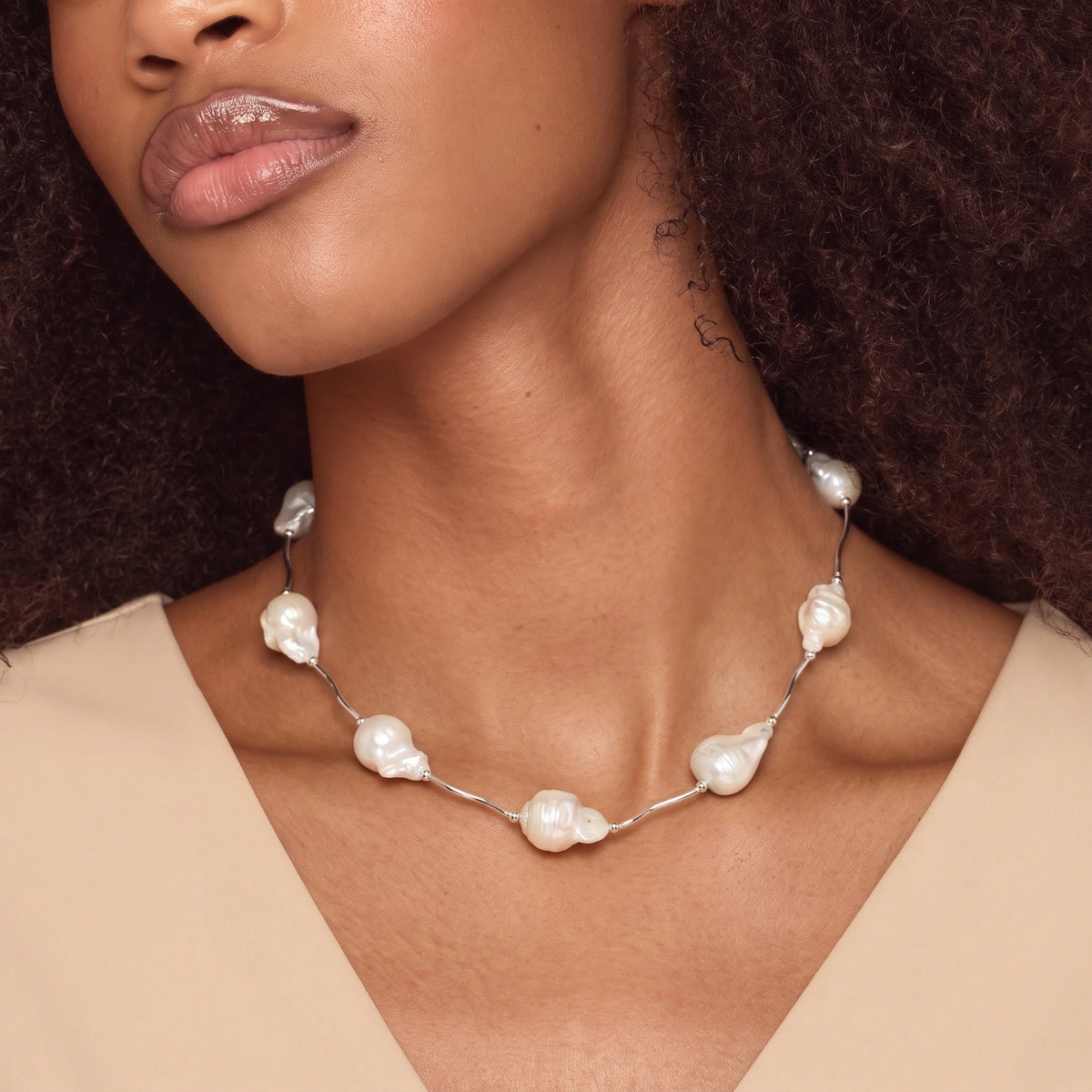 Woman wearing a necklace with silver tube links and scattered baroque pearls