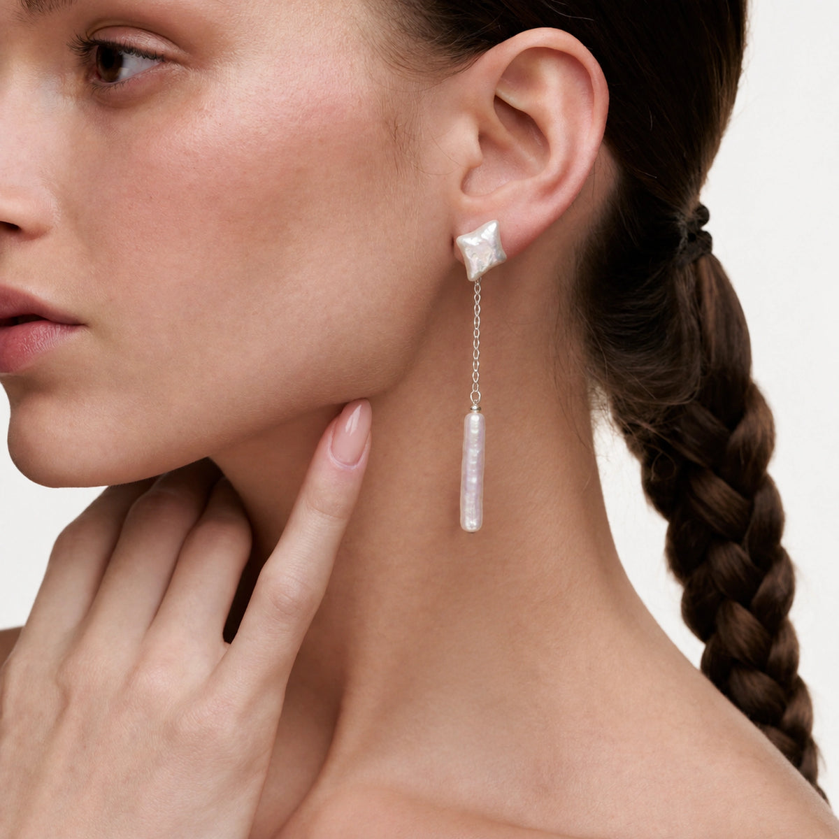 Woman wearing a silver star stud earring with a reed-shaped pearl drop, hand near neck