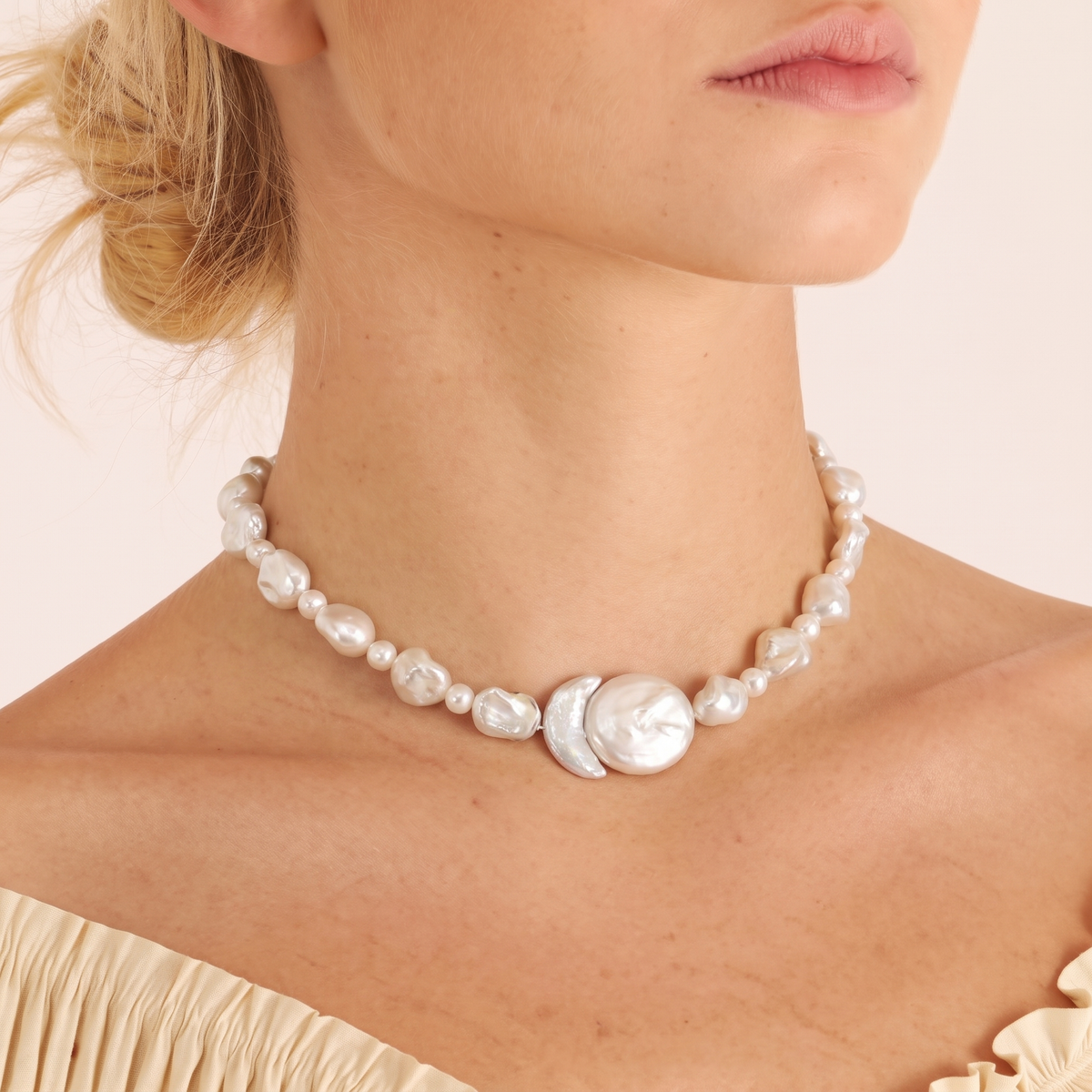 Woman wearing a pearl necklace with a crescent moon and round pearl centerpiece, updo hairstyle