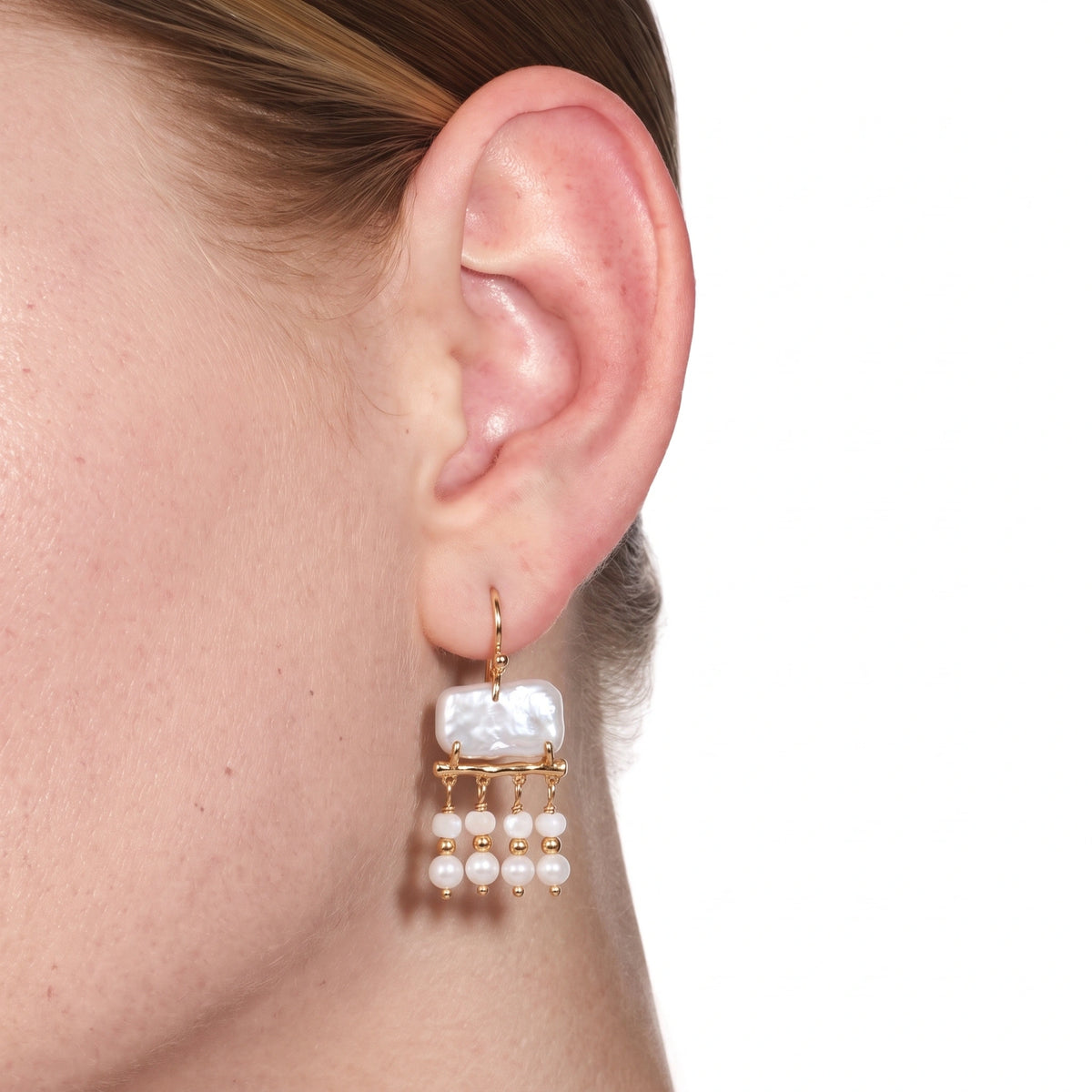 Close-up detail of a gold branch earring with pearl strand drops on a white background