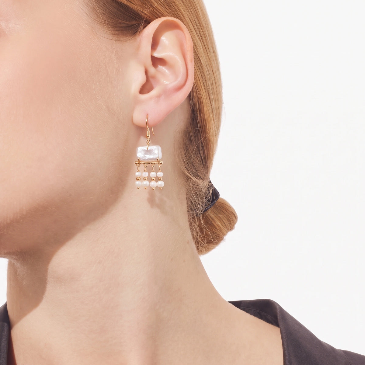 Side view of a gold branch earring with a rectangular pearl top and pearl strand drops, hair pulled back