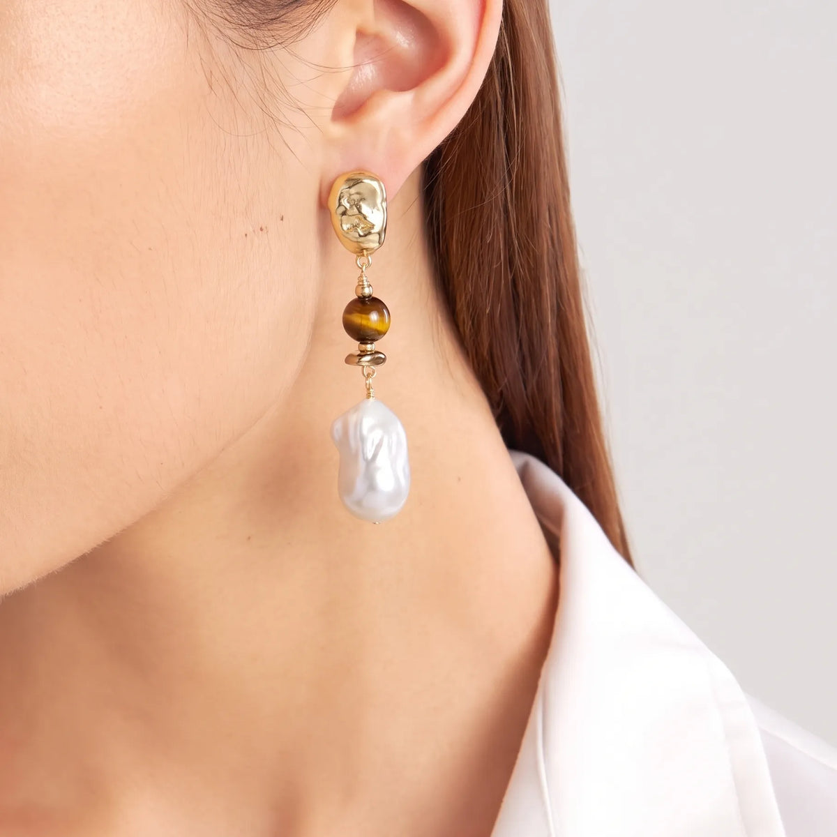 Close-up of a tiger eye and baroque pearl drop earring with hammered gold stud