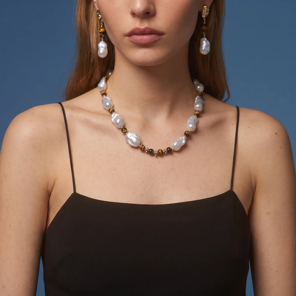 Woman wearing tiger eye and baroque pearl drop earrings with matching necklace