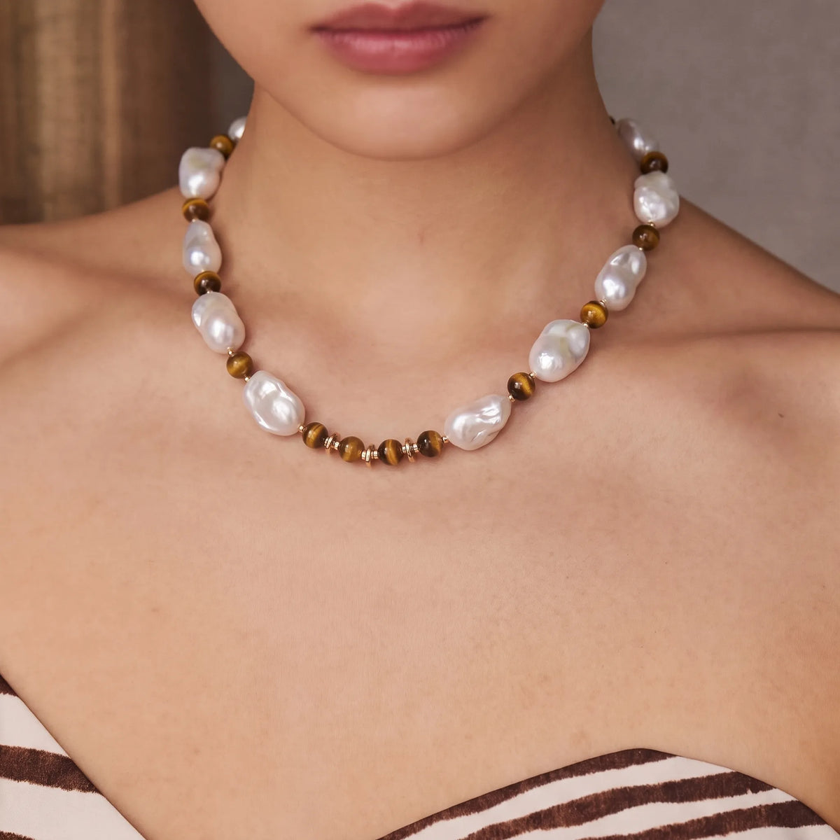 Side view of a tiger eye and baroque pearl beaded necklace with gold accents