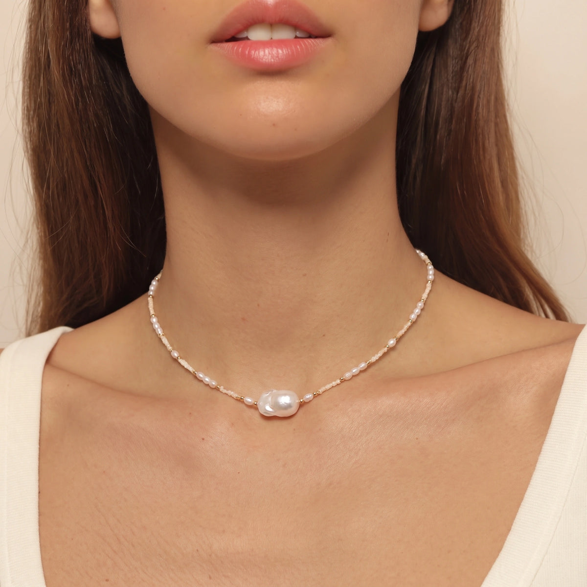 Woman wearing a delicate seed pearl necklace with a baroque pearl pendant