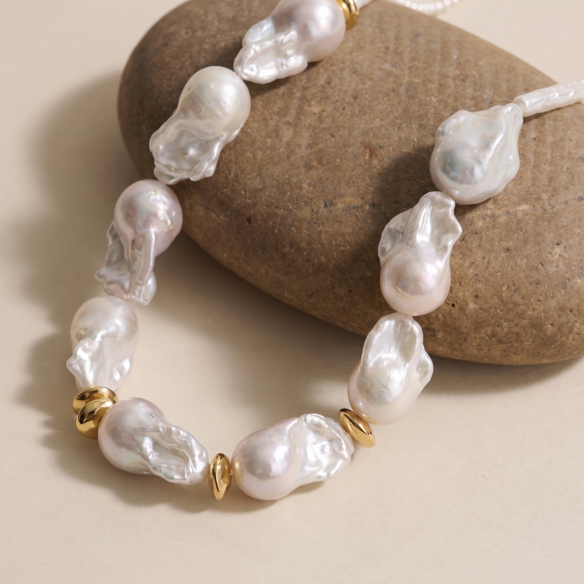 Close-up of baroque pearls and gold ring spacers on a necklace displayed on pebbles