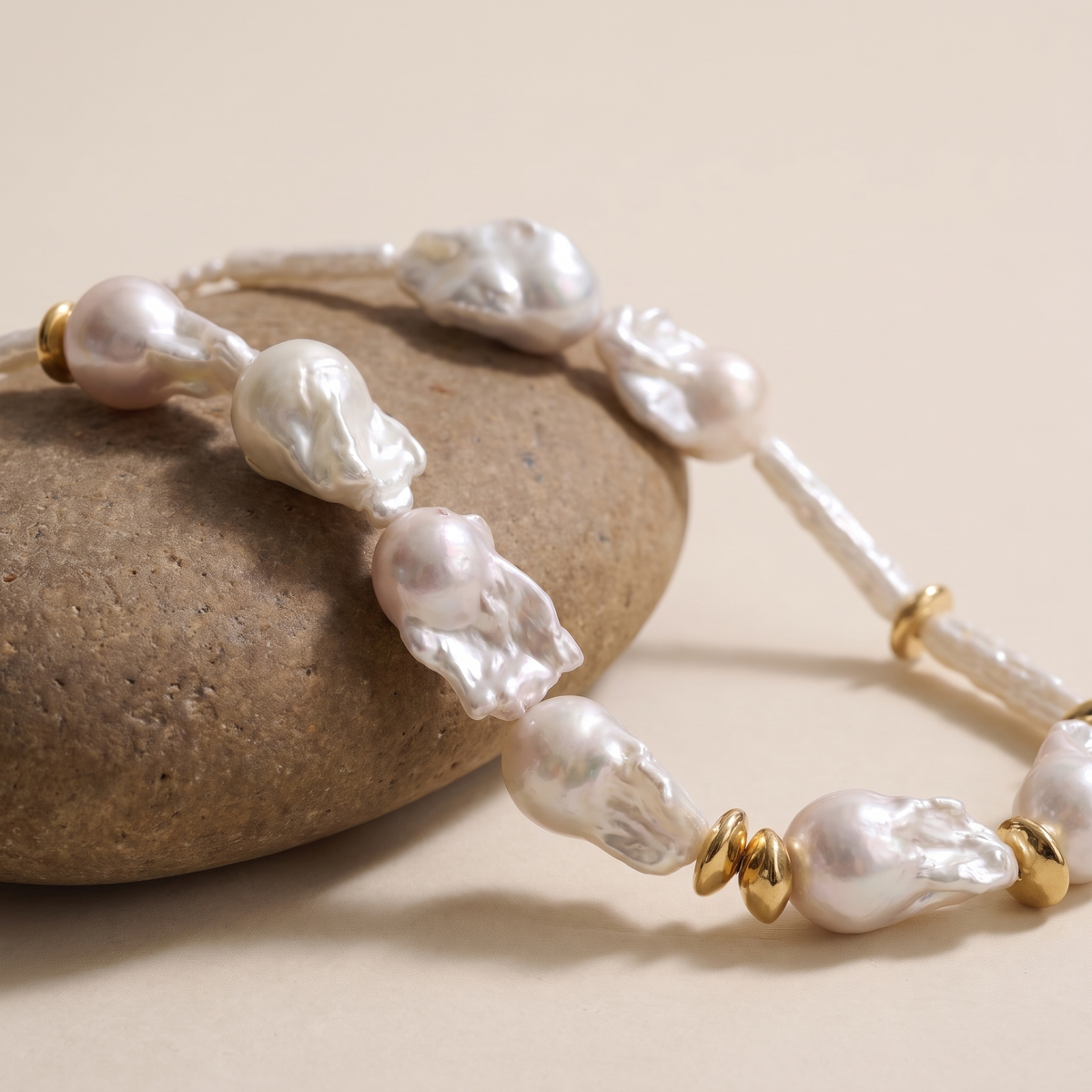 Baroque pearl necklace with gold ring spacers displayed on pebbles